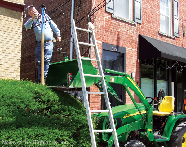 Photo by Jason Kaplan Unable to reach over the bush with a ladder, Gary Melrose used a tractor to reach the pole on which his Main Street business sign rests. Melrose spray painted the pole before reattaching the sign. 